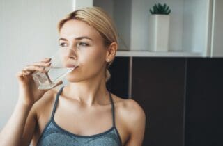 Woman drinking a glass of water in athletic top dry mouth xerostomia general dentistry dentist in Charleston North Carolina